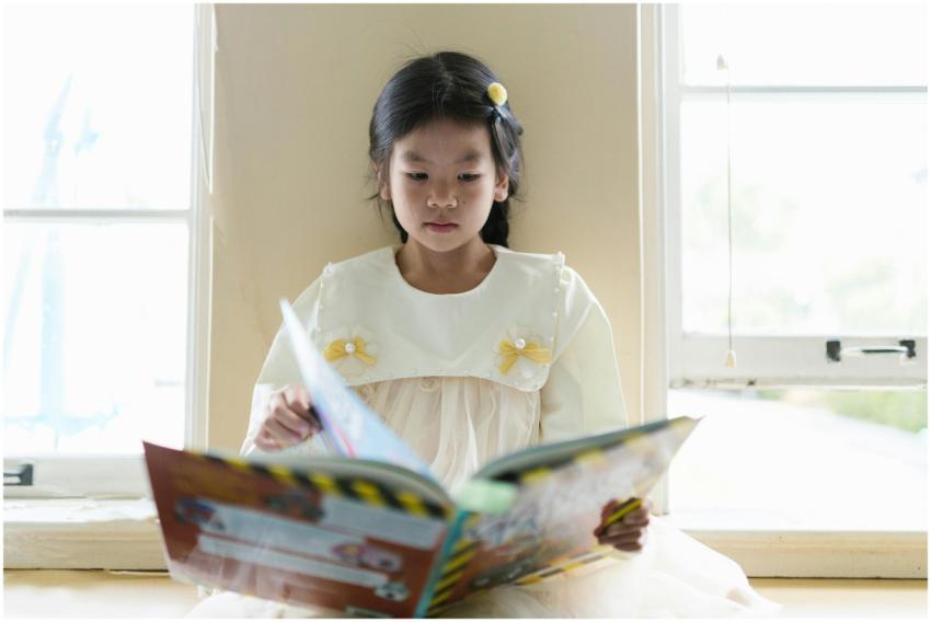 A young girl in a dress enjoys reading a book by a