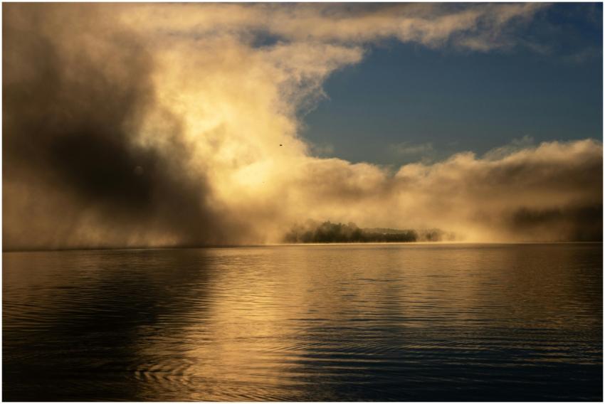 A serene lake enveloped in dramatic morning fog wi