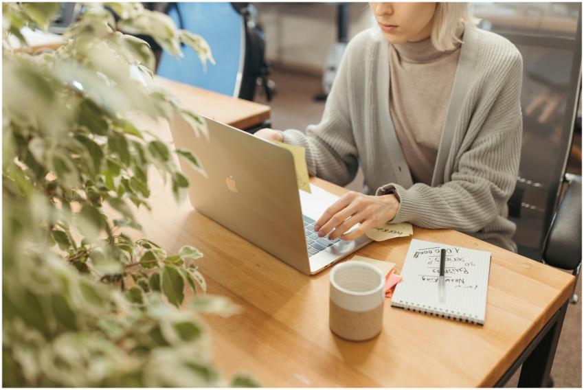 A woman working on a laptop at a wooden desk in a