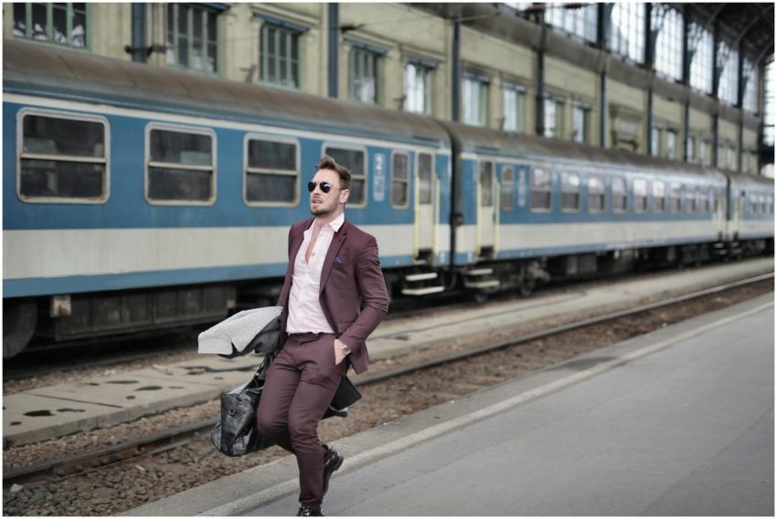 A man in a suit leans against a train platform, ex