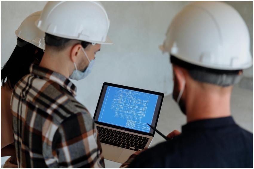 Engineers wearing hard hats and masks review a con
