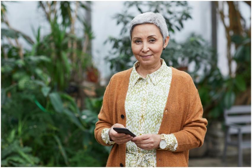 Elderly woman with smartphone standing in a greenh