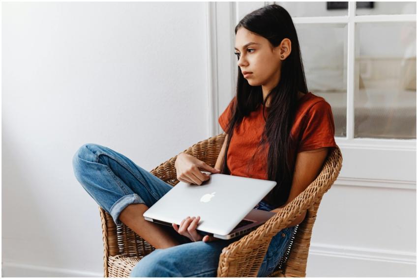 Teen girl indoors, lounging in a wicker chair, hol