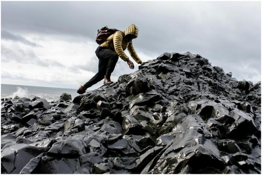 Person in yellow jacket climbs black rocky terrain