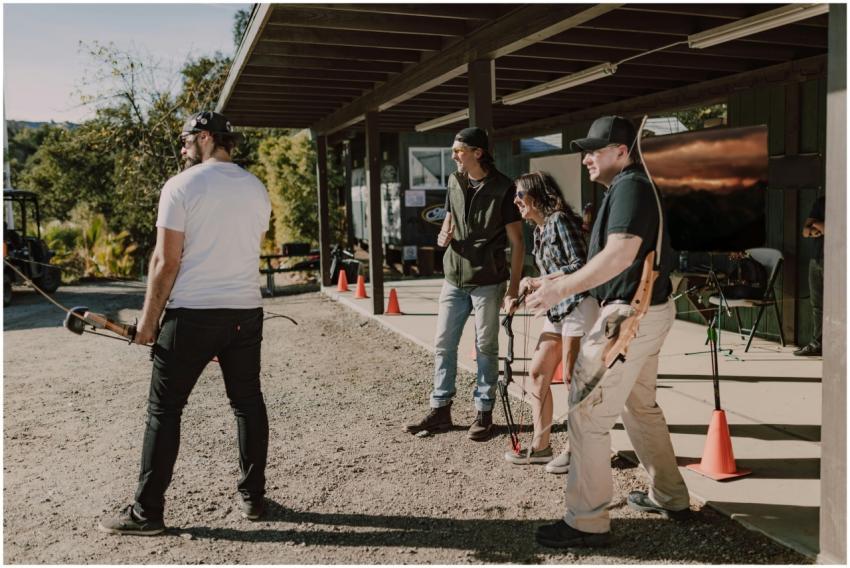 A group of adults practicing archery outdoors unde