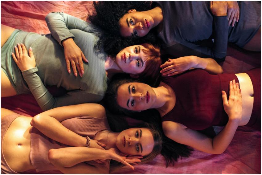 Empowered diverse women lying on pink fabric, show