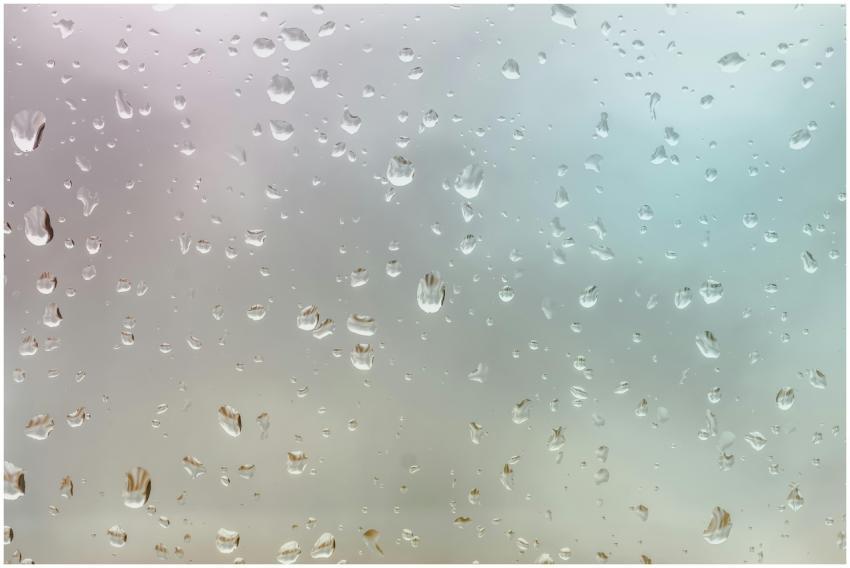 A close-up of raindrops on glass against a warm, s