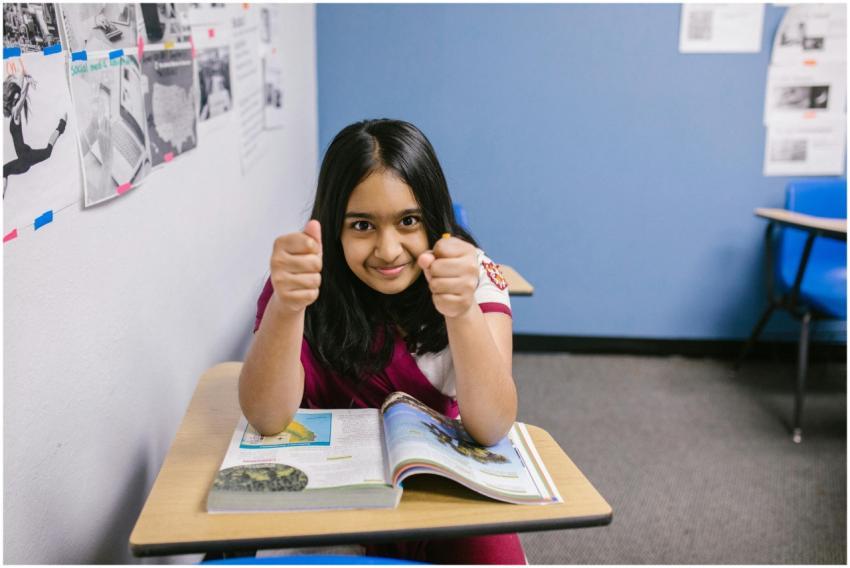 A confident young girl in a classroom giving a thu