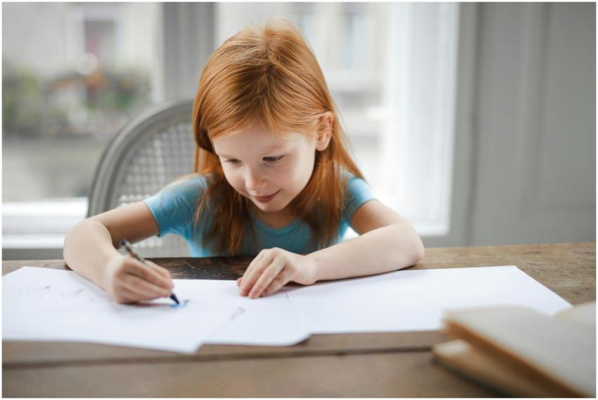 A young girl with red hair focused on drawing at a