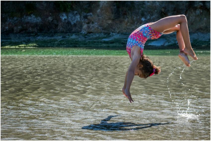 A young girl in a colorful swimsuit does a backfli