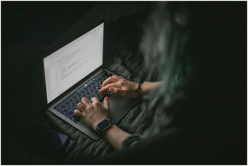 Close-up of hands typing on a laptop with code on