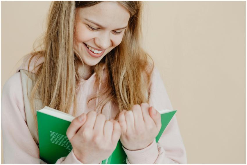 Happy teenager holding a green book against a beig