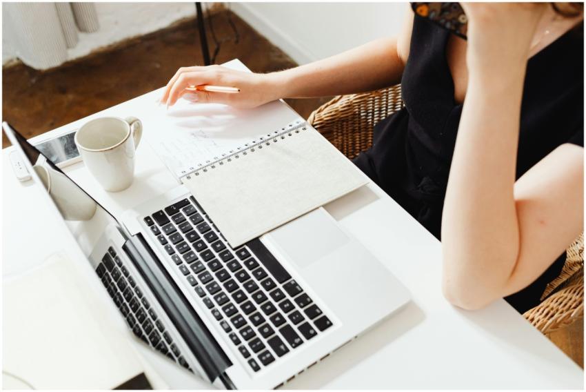 A woman writing notes while working on a laptop, i