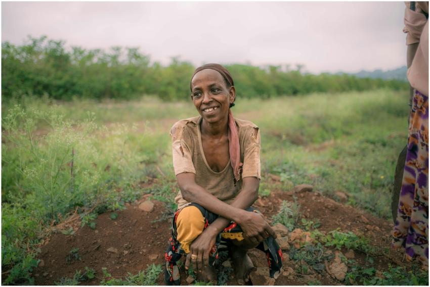 A cheerful Ethiopian woman sits in a green field,