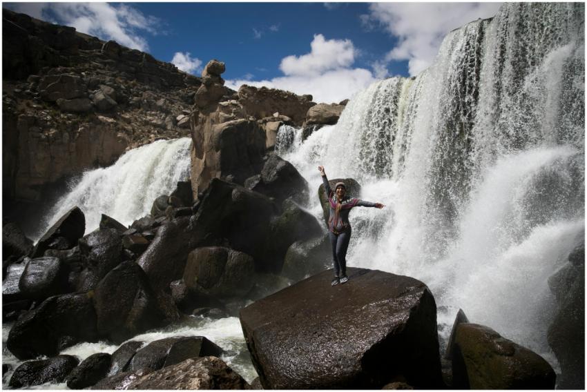 A woman posing confidently on rocks near a powerfu