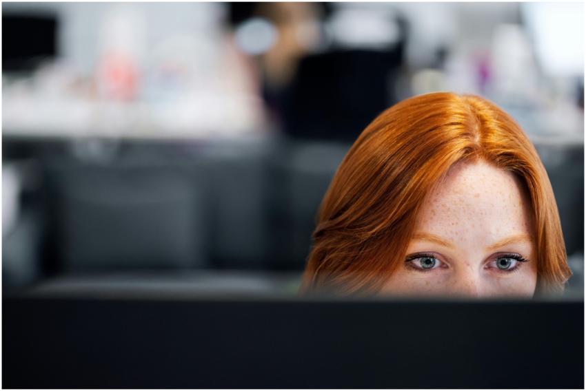 A woman with red hair intensely focused on a compu
