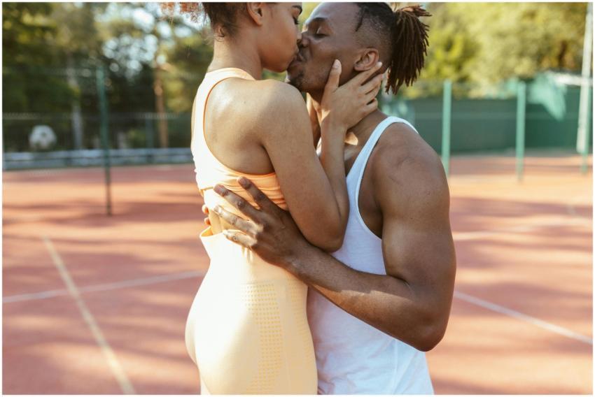 A couple embraces and kisses on an outdoor tennis