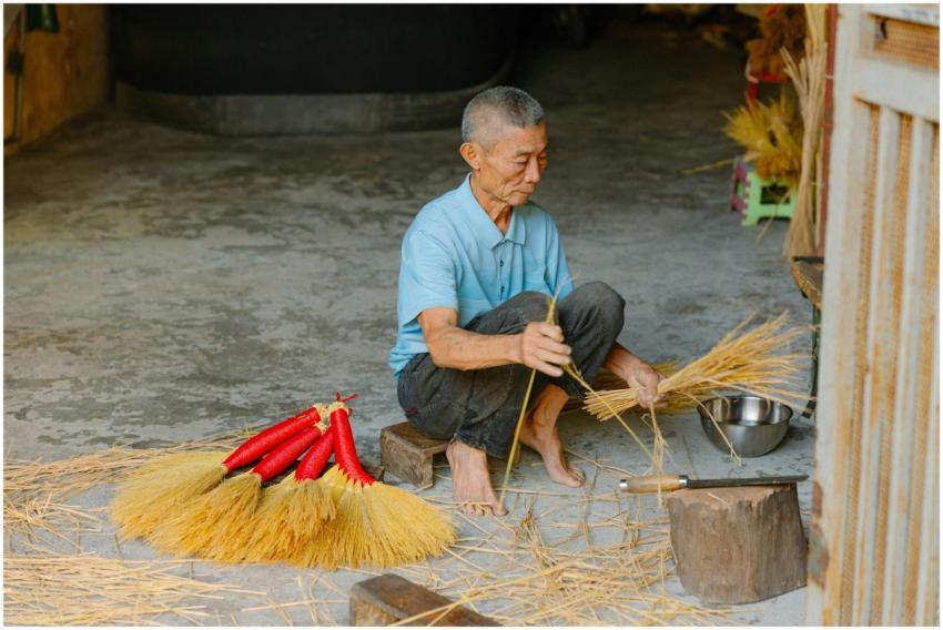 Asian elderly man crafting handmade brooms indoors