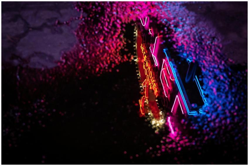 Colorful neon sign reflecting in a puddle on a dar