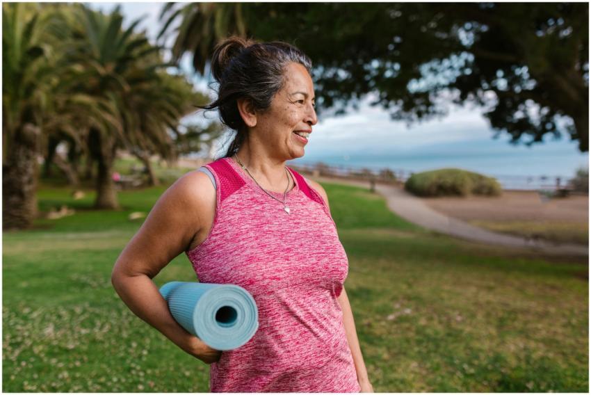 Smiling woman holding a yoga mat in a sunny park s
