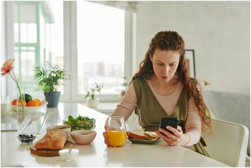 Pregnant woman at breakfast table browsing on smar