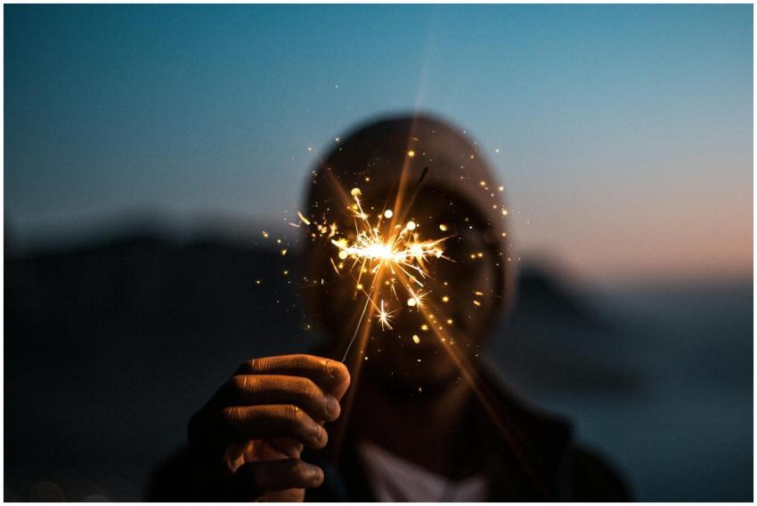 A silhouetted person holding a lit sparkler agains