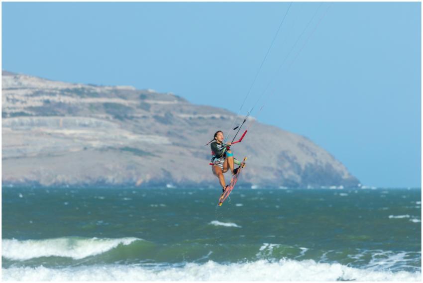A skilled female kitesurfer catches air over the o