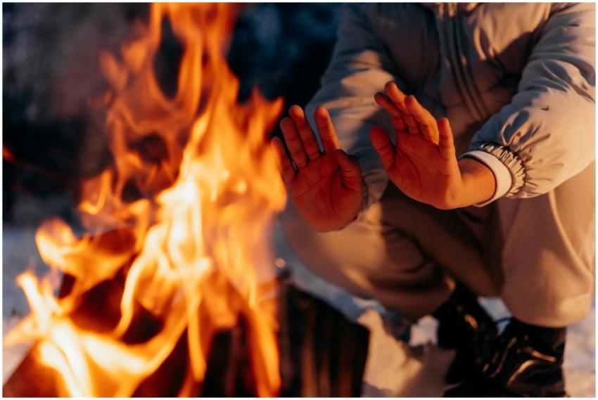 Close-up of hands being warmed by a campfire at ni