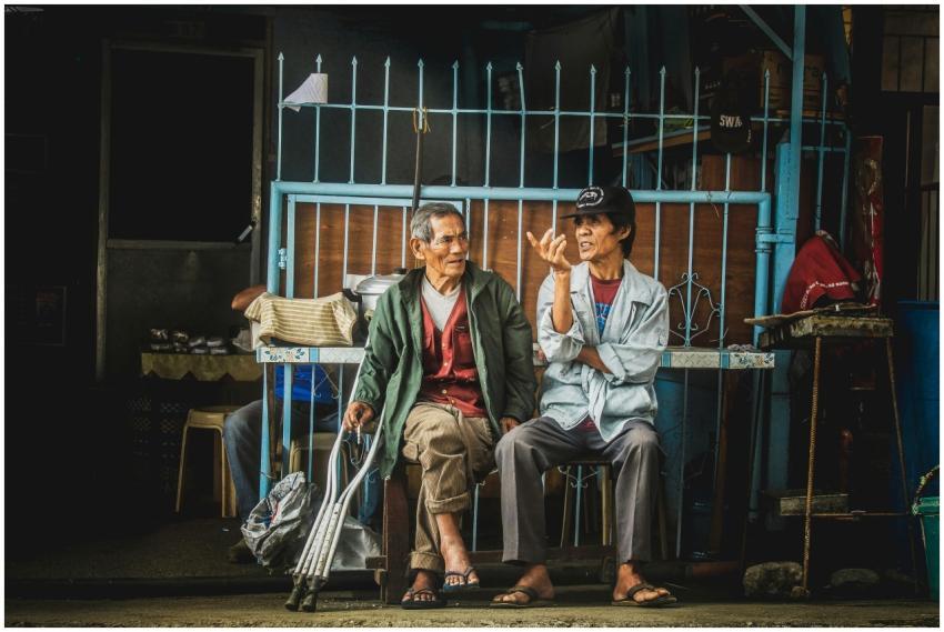 Two elderly men sit and converse outside a home in