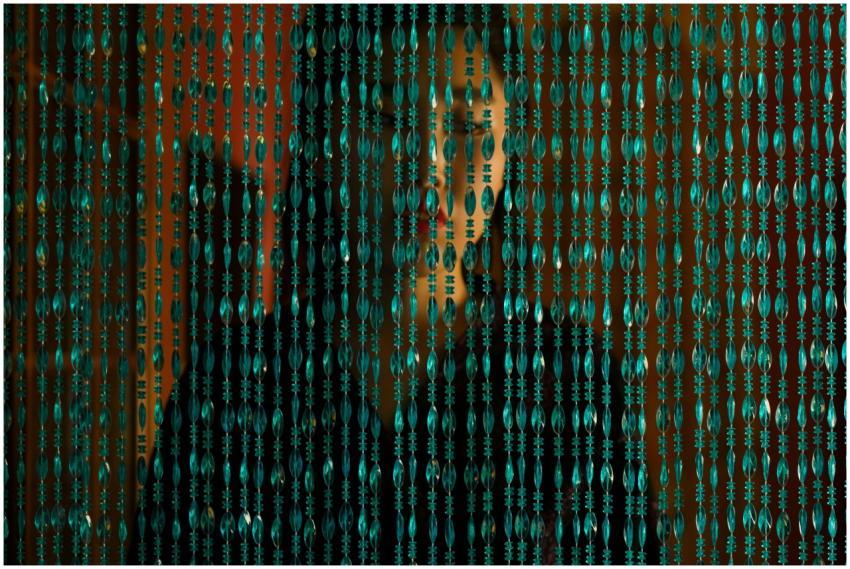 A woman stands behind a beaded curtain, creating a