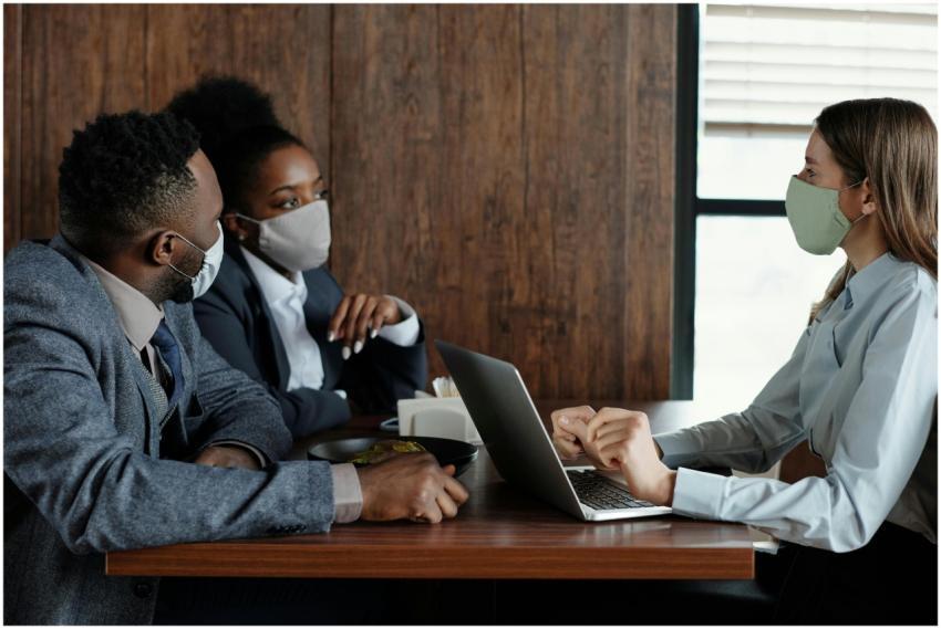 Three coworkers in masks discussing a project indo