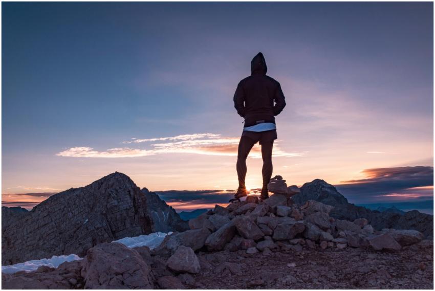 Person standing on a rocky mountain peak at sunset