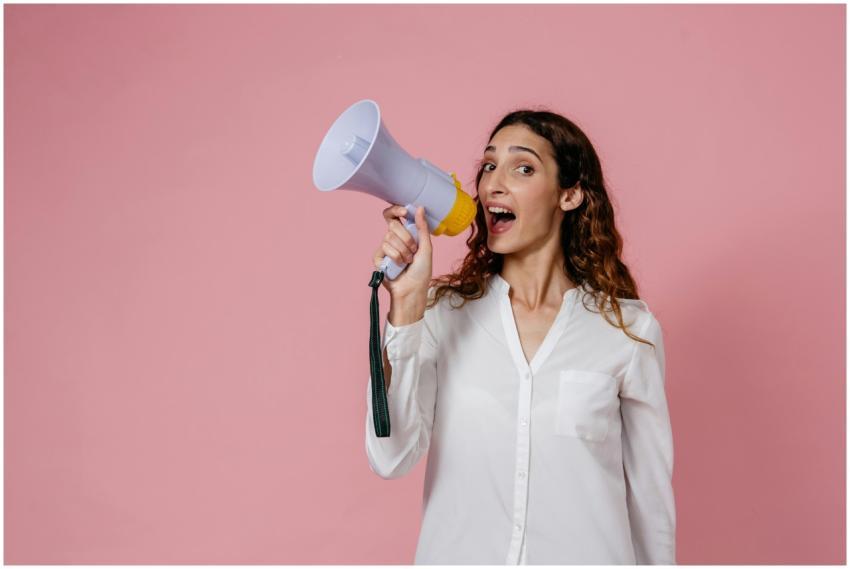 Woman in white shirt holding megaphone against a p