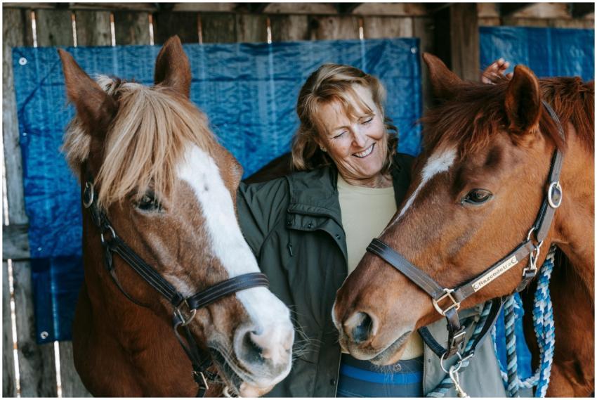 A joyful woman embraces two horses in a stable, sh