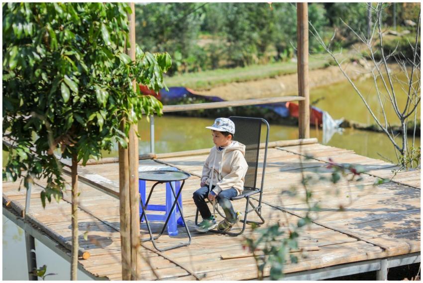 A young boy sits comfortably outdoors on a wooden