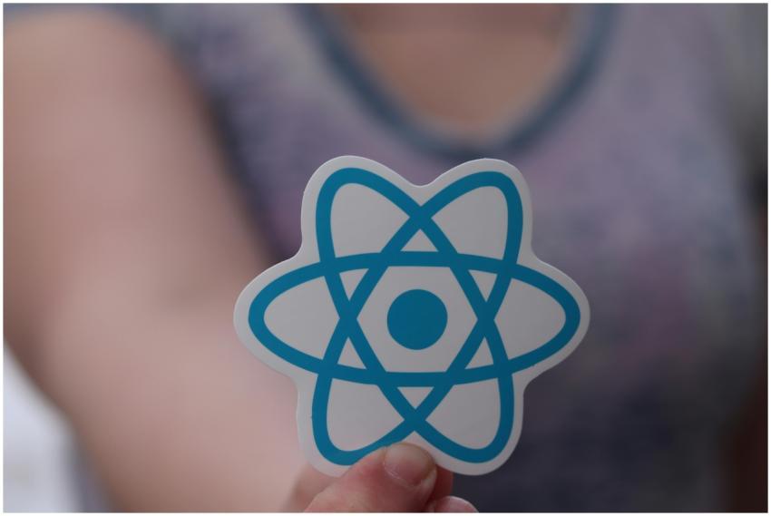A person holds a sticker featuring the React logo,