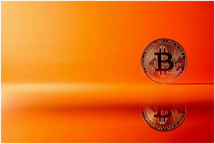 Golden Bitcoin with reflection on a bright orange