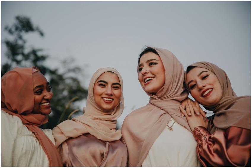 Four diverse women in hijabs laughing together out