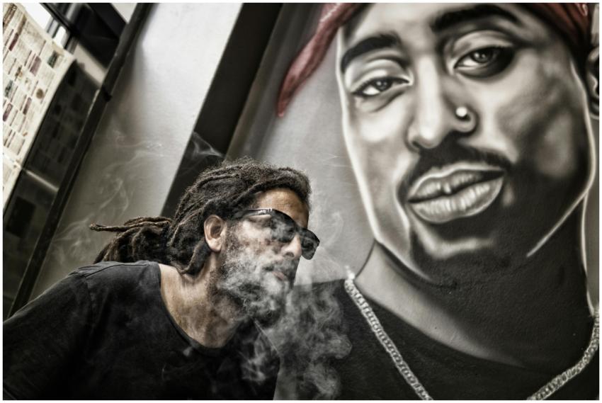 A man smoking in front of a mural featuring a hip