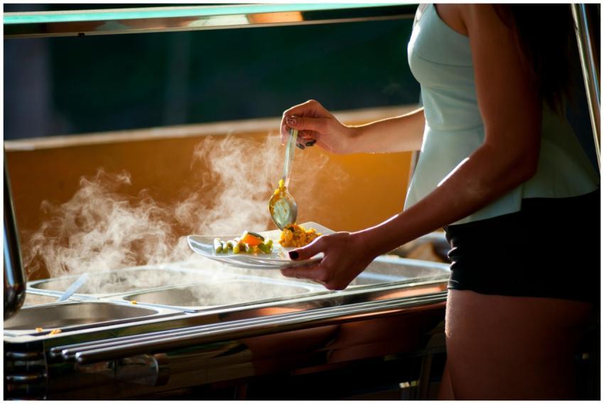 A woman serves steaming hot food in an indoor buff