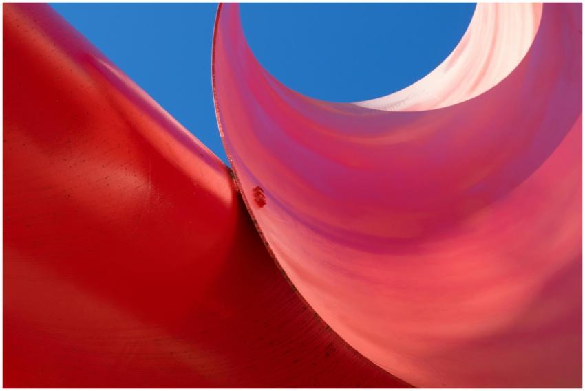 Abstract view of a red curved sculpture with a bri