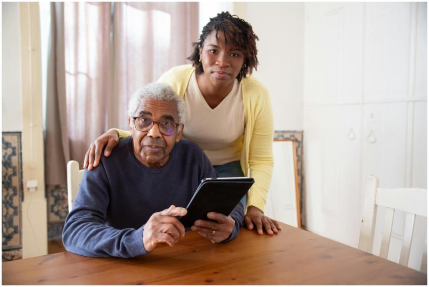A senior man with eyeglasses and caregiver using a