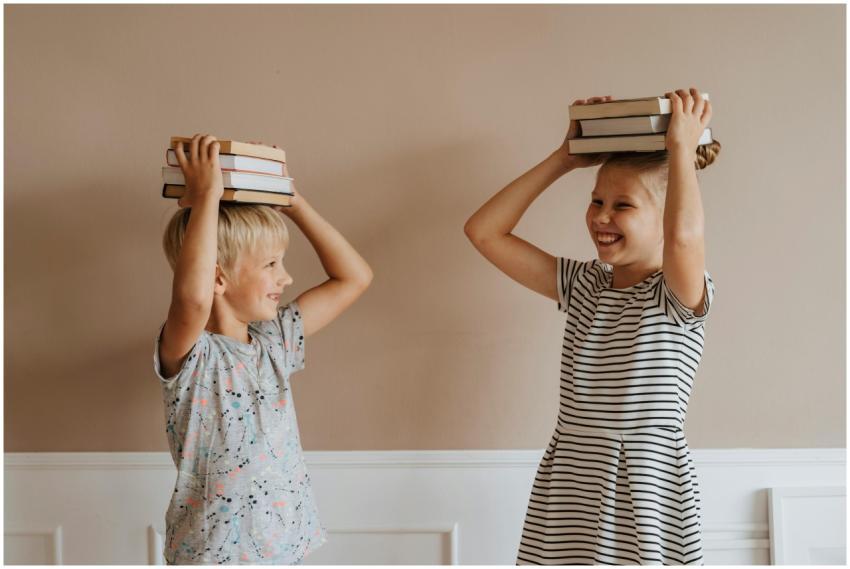 Two smiling children balancing books on their head