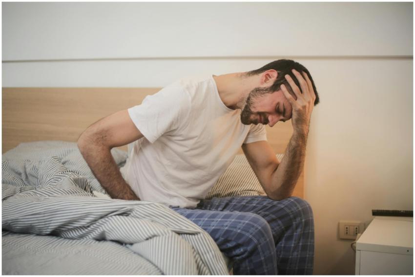 A young man in pajamas holding his head, sitting o
