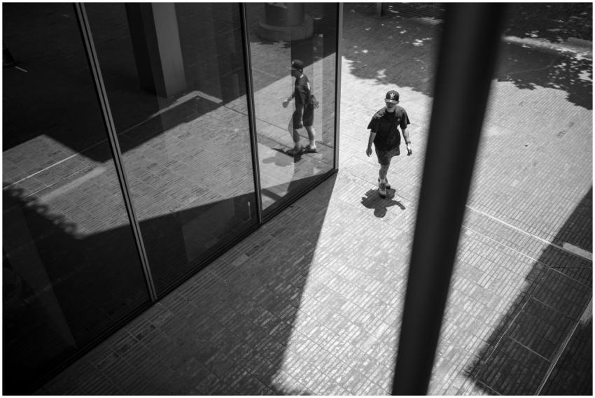 A person walks outdoors reflected in a modern glas