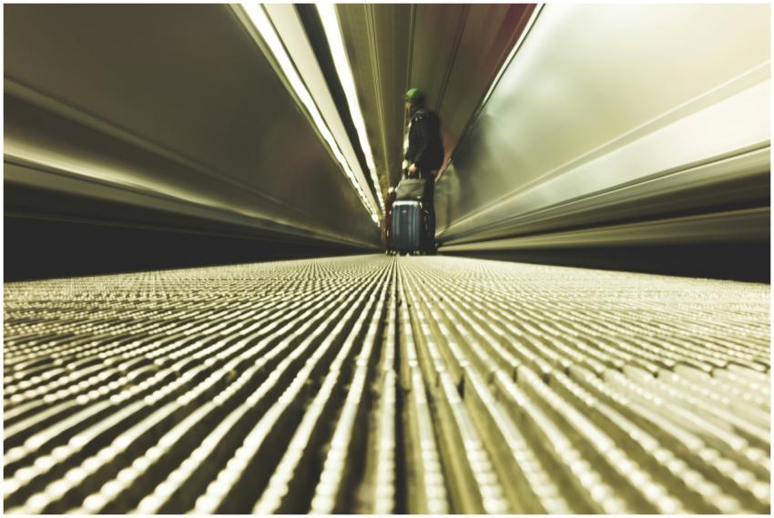 A traveler with luggage on a moving walkway in a m