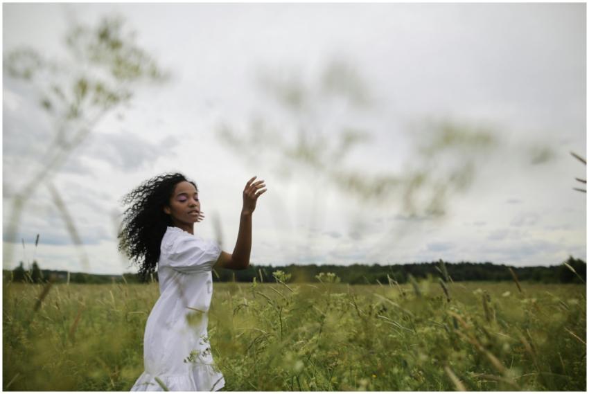 A woman in a white dress dances in a lush green me