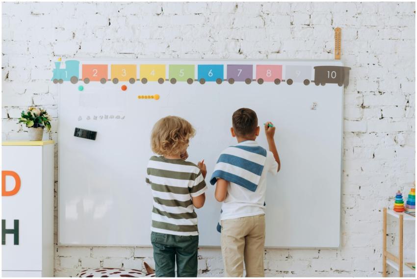 Two boys writing on a colorful classroom whiteboar