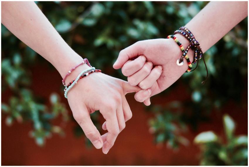 Two hands with colorful bracelets interlocked, sym