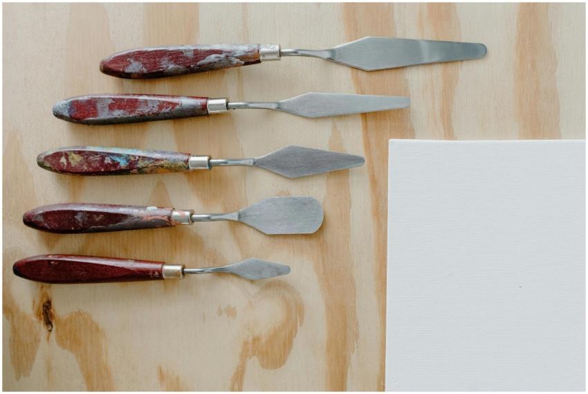 A set of five paint-covered palette knives on a wo